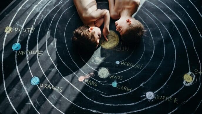 High-angle shot of two shirtless siblings lying on a colorful chalk drawing.