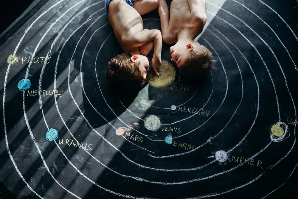 High-angle shot of two shirtless siblings lying on a colorful chalk drawing.