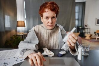 A mature woman sits at a desk in her living room, speaking to a doctor via video call.
