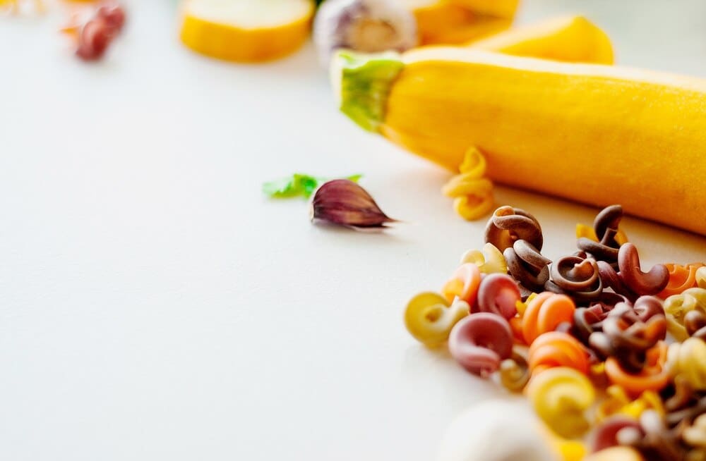 Close-up of ingredients for pasta, including tomatoes, spinach, and carrots, representing natural dyes.