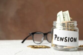 A glass jar filled with money has the word "Pension" written on it, set against a brown background.