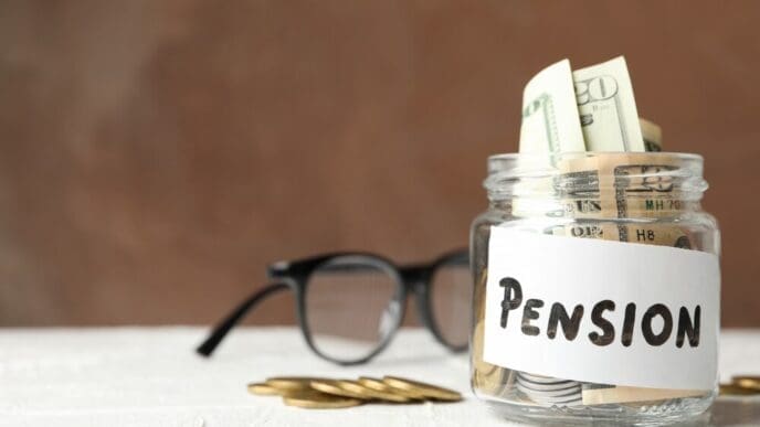 A glass jar filled with money has the word "Pension" written on it, set against a brown background.
