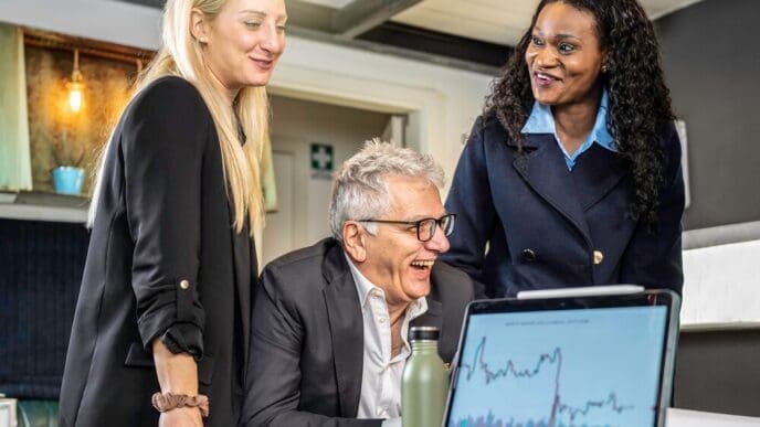 A diverse business team smiles while reviewing market trends on a computer during a meeting.