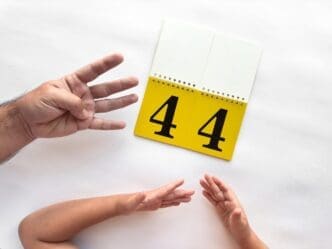 A person uses hand gestures to demonstrate numbers while holding up number flashcards.