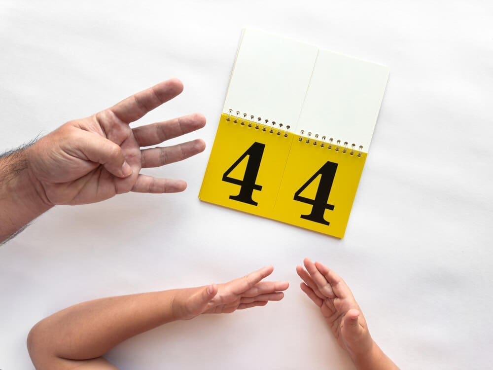 A person uses hand gestures to demonstrate numbers while holding up number flashcards.