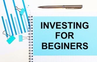 Overhead view of light blue diagrams, paper clips, and a sheet of paper labeled "INVESTING FOR BEGINNERS" on a light surface, representing a business concept.