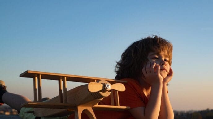 A young boy plays with a wooden airplane, dreaming of becoming a pilot or astronaut.