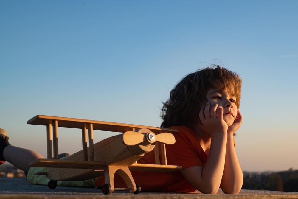 A young boy plays with a wooden airplane, dreaming of becoming a pilot or astronaut.