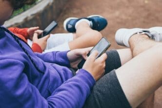 Close-up of several male friends sitting outside and using their phones.
