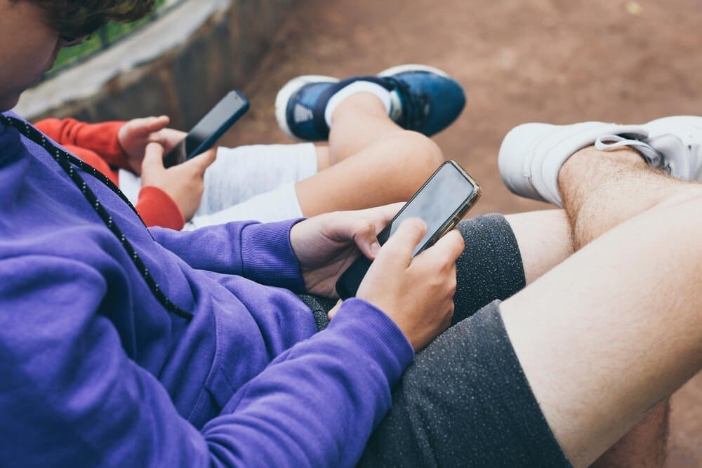 Close-up of several male friends sitting outside and using their phones.