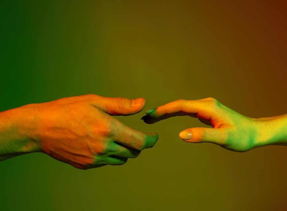 Hands of a man and woman reach toward each other, set against a red and green neon-lit background.