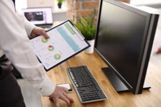 A man's hand holds charts displaying commercial indicators in a workplace setting, illustrating business development.