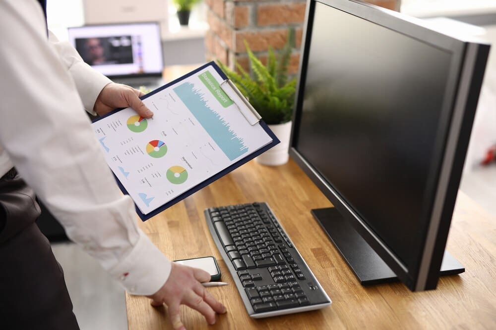 A man's hand holds charts displaying commercial indicators in a workplace setting, illustrating business development.