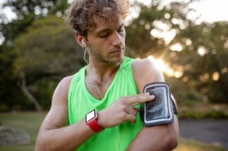 A man wearing athletic clothing jogs while listening to music on his mobile phone.