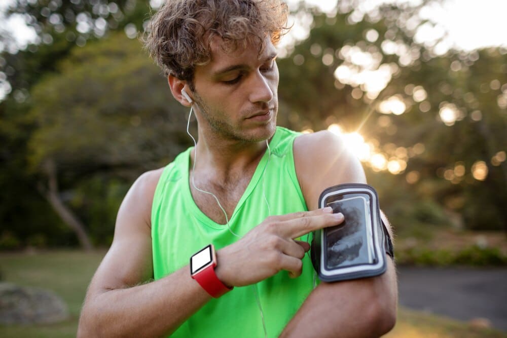 A man wearing athletic clothing jogs while listening to music on his mobile phone.