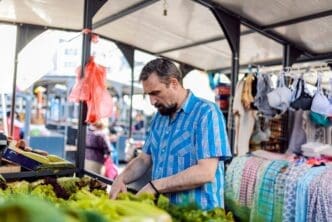 A man with a beard and plaid shirt selects vegetables at a market.