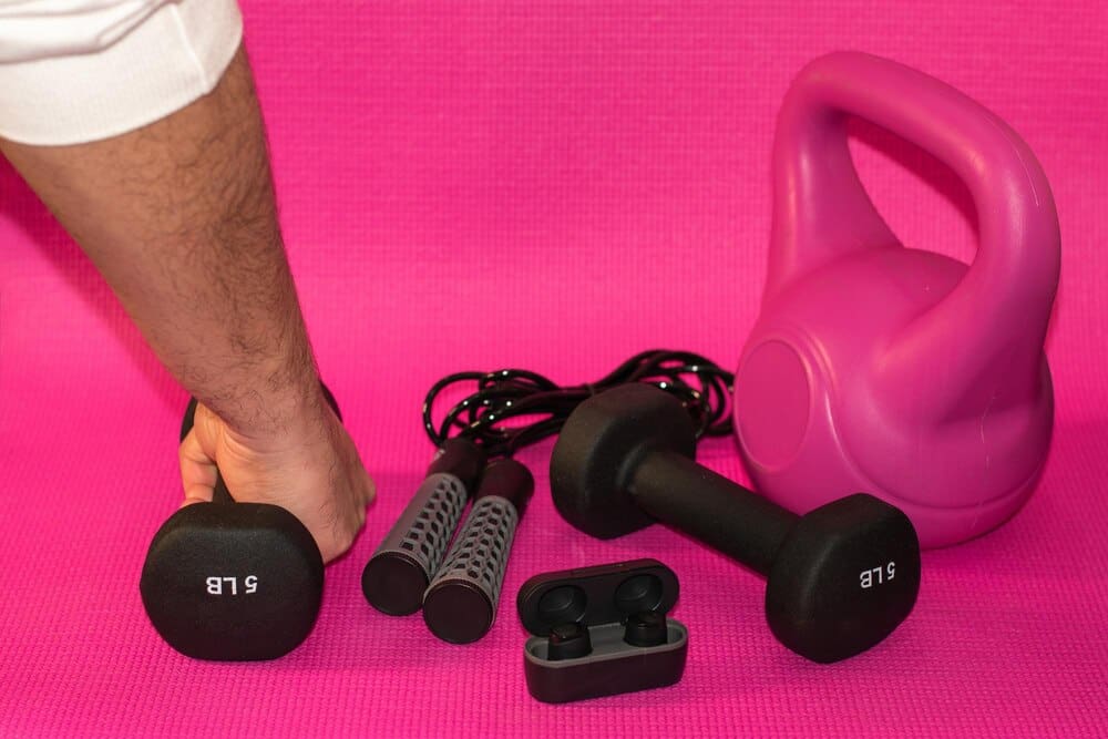 A man holds dumbbells in front of a pink background with the letters "btt."