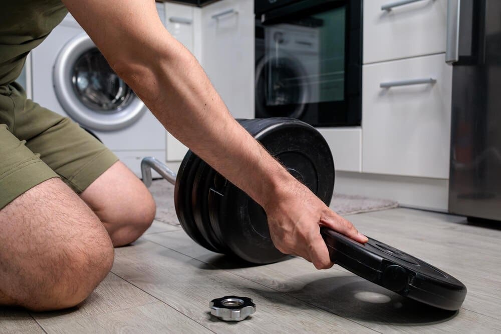 A man is attaching an insulator to his pants while a barbell with weights rests on the floor.