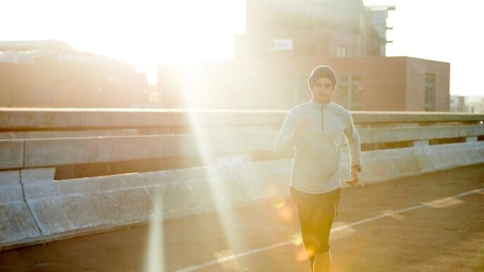 A man runs on a road at sunrise, exercising outdoors for fitness training and health, with a bridge and metro street in the background.
