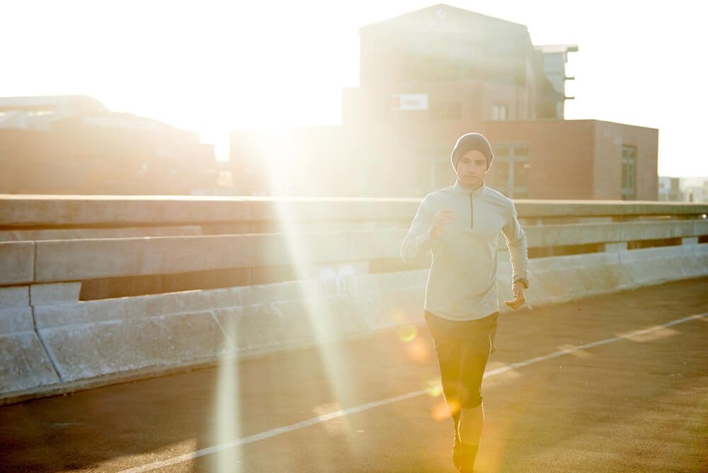 A man runs on a road at sunrise, exercising outdoors for fitness training and health, with a bridge and metro street in the background.