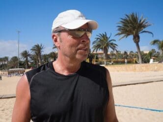 A man wearing sunglasses stands on a beach with the sky in the background.