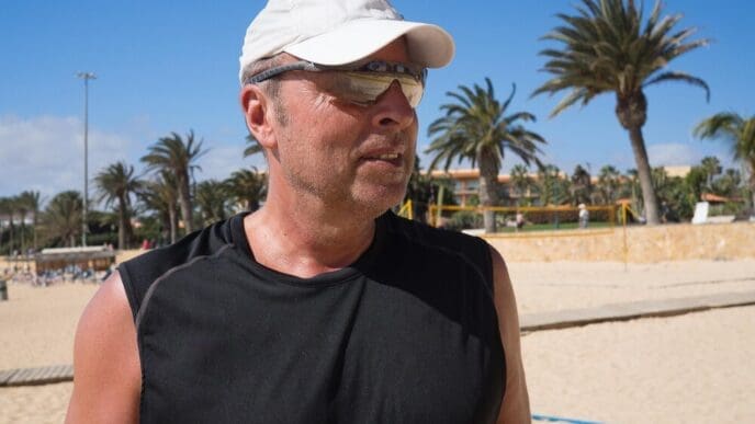 A man wearing sunglasses stands on a beach with the sky in the background.