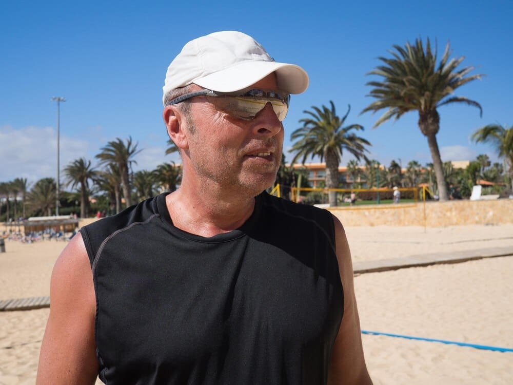 A man wearing sunglasses stands on a beach with the sky in the background.