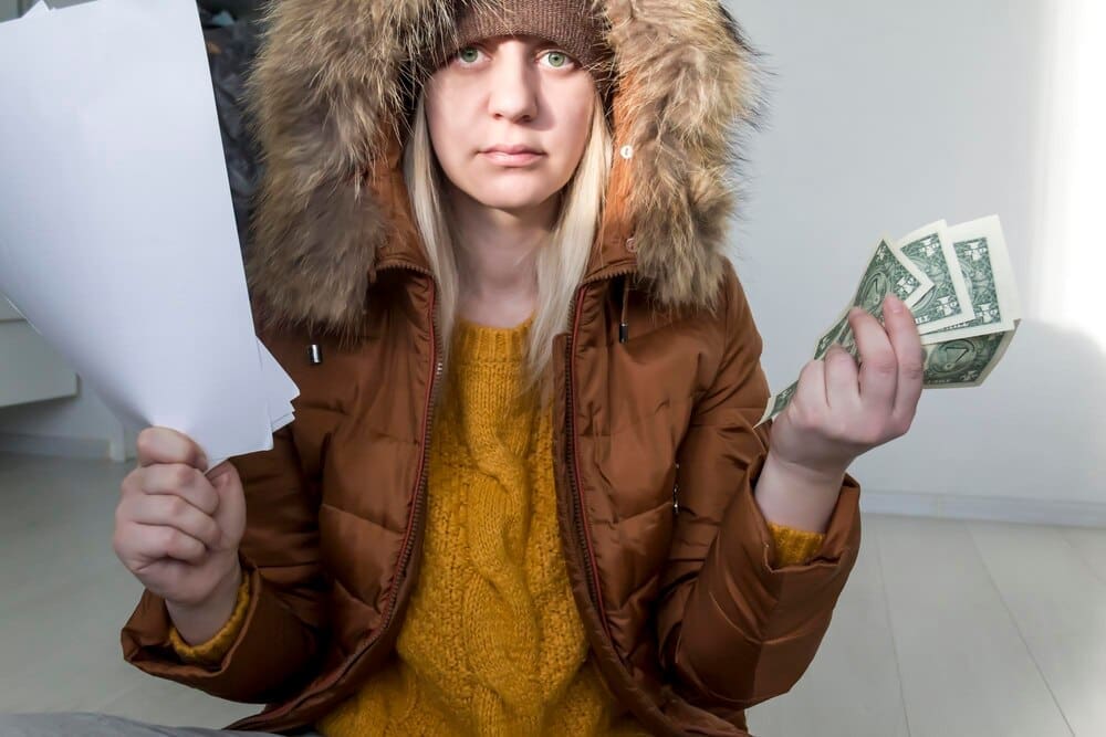 A man in a yellow sweater and jacket holds documents and money, illustrating the concept of economic crisis and high utility bills.