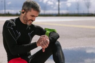 A mature man sits on a road, looking at his wristwatch.