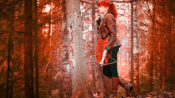A mature model with red curly hair poses as a royal huntress, aiming a crossbow in a forest setting.