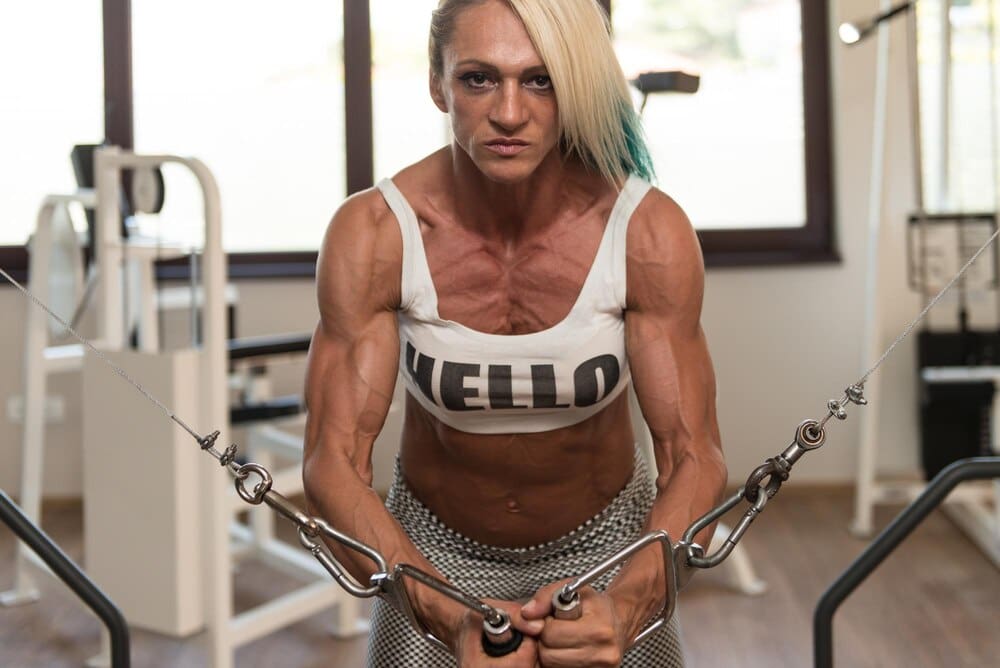 A mature woman exercises her chest using a cable crossover machine in a gym.