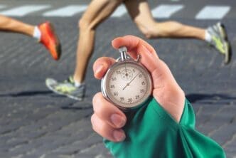 A close-up shows a hand holding a mechanical stopwatch, with the legs of a runner blurred in the background.