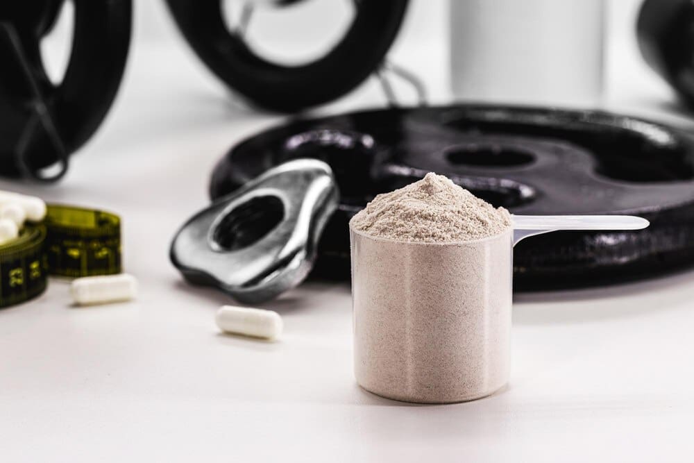 A measuring spoon scoops a white powder, possibly a supplement, next to a container, suggesting a bodybuilding or nutritional concept.