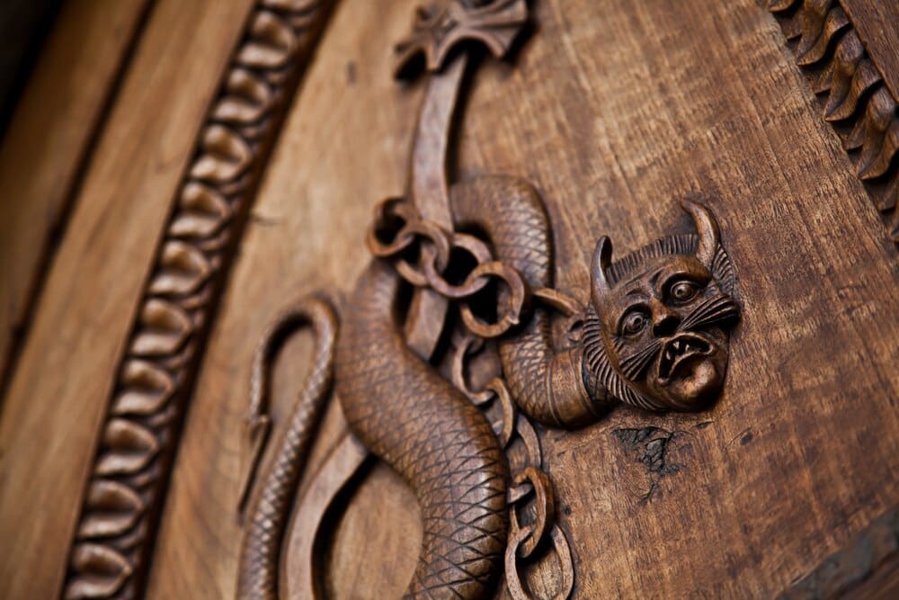 A detailed carving of a medieval demon adorns an antique wooden door.