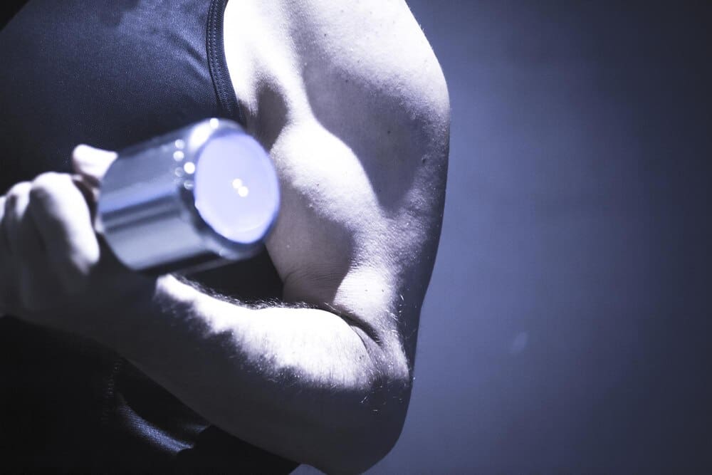 A muscular man holds a dumbbell overhead against a black background.
