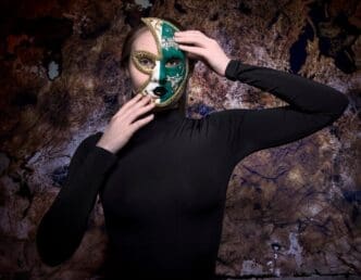Midsection of a person wearing a half-mask stands against a wall.