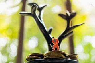 Miniature figures work on a stack of coins beneath a tree-like structure, symbolizing business concepts.