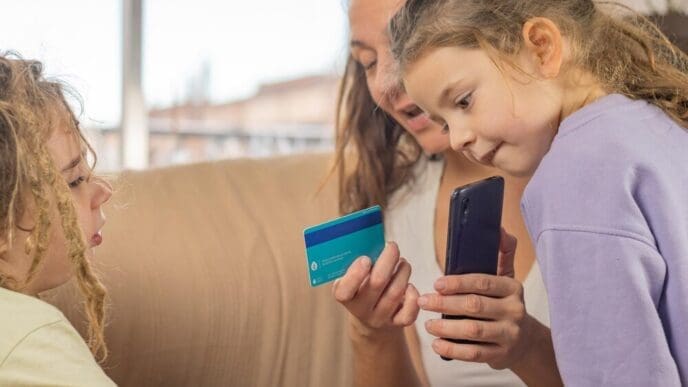 A mother with a bank card and smartphone demonstrates financial technology to her two young sons with dreadlocks.