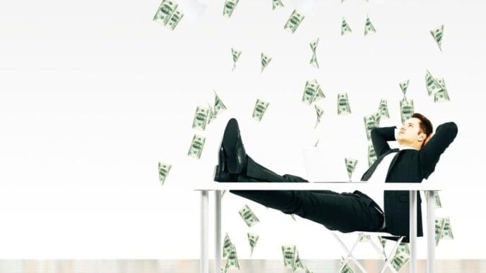 A businessman sits in a chair beneath a cloud raining money.