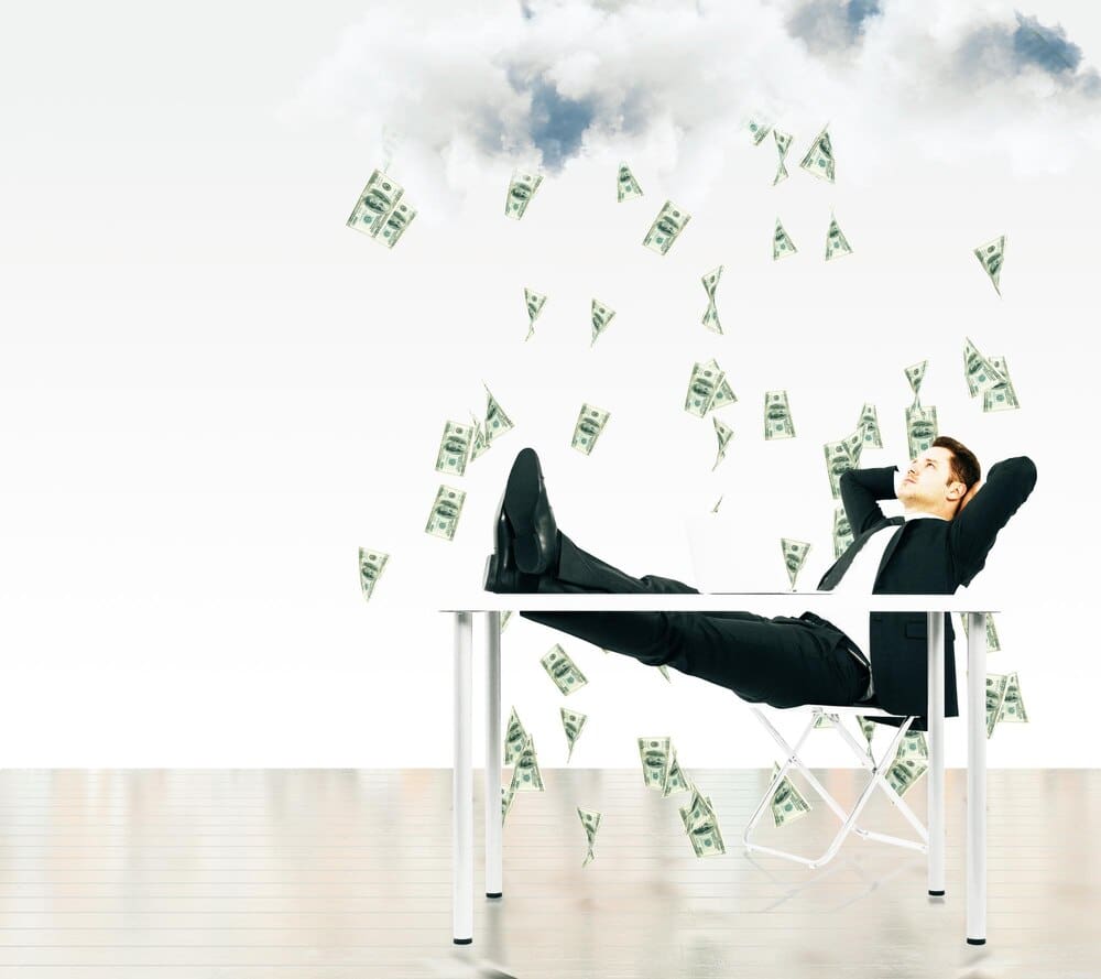 A businessman sits in a chair beneath a cloud raining money.