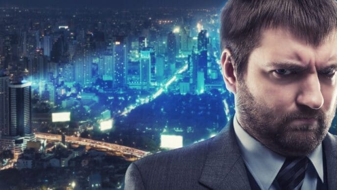 A somber businessman stands in front of a brightly lit cityscape at night.