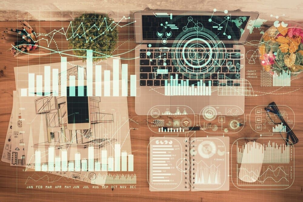 Overhead view of a table with a laptop, a pen, and a financial chart overlaid on the background.