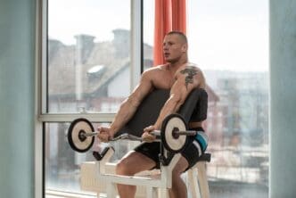 A muscular man curls a barbell to exercise his biceps.
