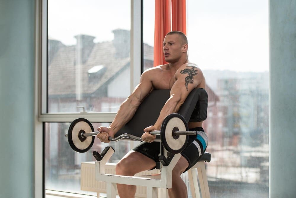 A muscular man curls a barbell to exercise his biceps.