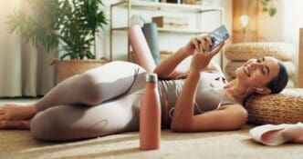 A woman listens to a zen audio podcast on her phone while practicing yoga at home.