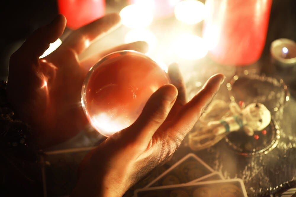 A still life featuring a voodoo doll, tarot cards, books, candles, and other objects associated with witchcraft.