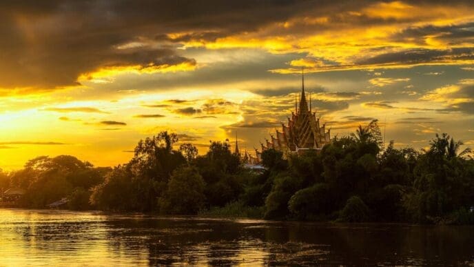 A serene evening scene shows a temple complex reflected in the Nan River at Raft Village in Phitsanulok, Thailand.