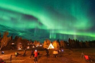 The night sky above Aurora Village in Yellowknife, Northwest Territories, Canada, is illuminated by the vibrant green and purple colors of the aurora borealis.