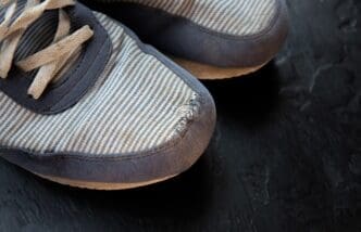 A pair of old, dirty, and worn-out sneakers has a hole in one of them.
