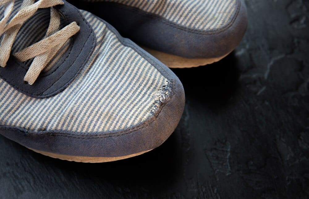 A pair of old, dirty, and worn-out sneakers has a hole in one of them.